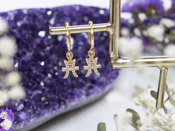 HUGIE DE SIGNO PISCIS CON CRISTAL SWAROVSKI MORADO, CON CHAPA DE ORO EN 14 KILATES.